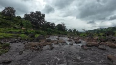 Ormandaki kayaların üzerinden akan sakin bir akarsu manzarası, doğanın rahatlatıcı seslerini ve canlı yaprakları sergiliyor.