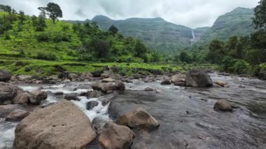 Ormandaki kayaların üzerinden akan sakin bir akarsu manzarası, doğanın rahatlatıcı seslerini ve canlı yaprakları sergiliyor.
