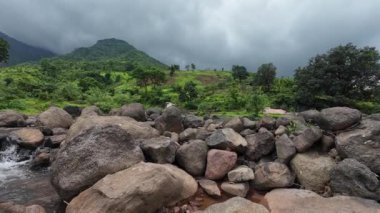 Ormandaki kayaların üzerinden akan sakin bir akarsu manzarası, doğanın rahatlatıcı seslerini ve canlı yaprakları sergiliyor.