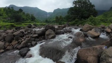 Ormandaki kayaların üzerinden akan sakin bir akarsu manzarası, doğanın rahatlatıcı seslerini ve canlı yaprakları sergiliyor.