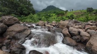 Ormandaki kayaların üzerinden akan sakin bir akarsu manzarası, doğanın rahatlatıcı seslerini ve canlı yaprakları sergiliyor.