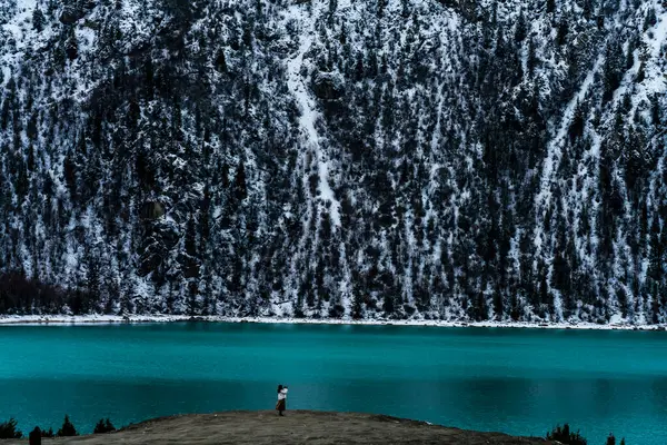 Mavi elbiseli bir adamın gölün yakınındaki bir kayanın üzerinde dikey görüntüsü.