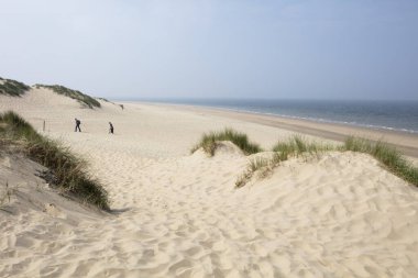 Dunes and the north sea coastwith two unsharp (motion blur) walkers in Burgh Haamstede in the Netherlands clipart