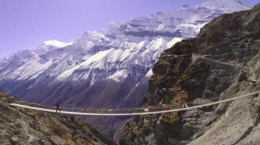 Person walking over bridge through the Himalaya mountains in Nepal viewing snow  on the peaks.