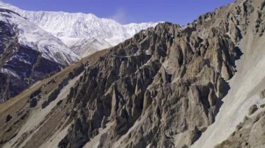 Manang Nepal 'deki sarp kayalıklar boyunca uçuyor. Uzakta karlı dağlar ve aşağıda patikalar var..