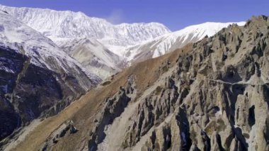 Manang Nepal 'deki sarp kayalıklar boyunca uçuyor. Uzakta karlı dağlar ve aşağıda patikalar var..