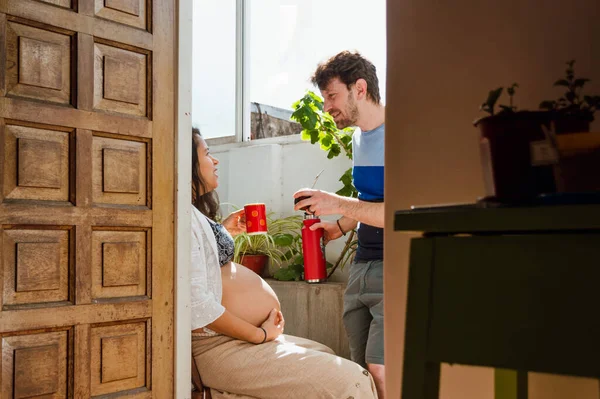 妊娠中のラテン系のカップルが熱い飲み物を飲んで家で話し家の中から玄関のドアを通って — ストック写真