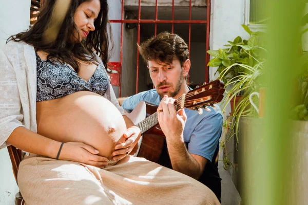 幸せな父親のクローズアップ 彼の妻の腹の中で彼の赤ちゃんに歌っている白人のアルゼンチンの若い男若い妊娠中のブラジル人女性 妊産婦と家族の概念 — ストック写真