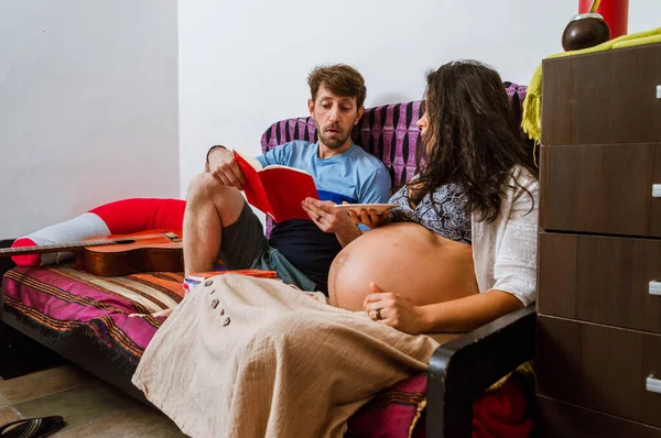 髭を生やした白人成人男性は室内で妊娠中の妻に本の中で物語を読むことに集中していますリビングルームに座ってライフスタイルの概念とコピースペース — ストック写真
