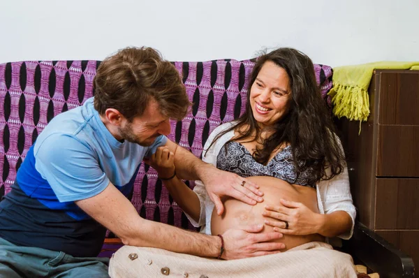 一个成年男子用双手触摸妻子的腹部 看着女儿在子宫里移动 坐在扶手椅上 他们笑着 快乐地等待着孩子的出生 — 图库照片