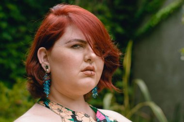 Arjantinli etnik kökenli Latin kökenli Latin kökenli genç bir kadının yakın plan portresi, ciddi bir yüzle bahçede duruyor ve dışarıdaki kameraya bakıyor..