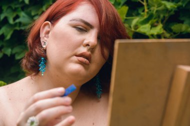 Kafkas kökenli, kısa kızıl saçlı, elinde mavi bir tebeşirle oturmuş resim yapmayı düşünen genç bir Latin kadının yakın çekimi.