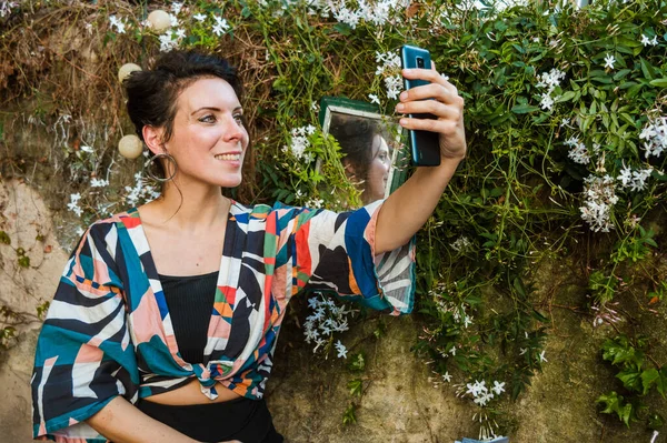 beautiful caucasian adult woman of French ethnicity, taking a selfie with her phone sitting on the terrace of her house, taking a photo to upload to social networks.