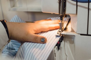 closeup of a female hand of caucasian woman, holding a cotton fabric that she is sewing with a professional sewing machine, entrepreneurship concept, copy space