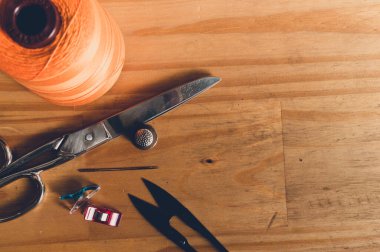 top view of roll of orange yarn with scissors placed on a wooden table with copy space on the right.