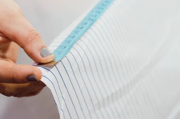 close-up of a female hand extending a tape measure along the edge of a fabric, measuring the length she needs for the clothing she is making.