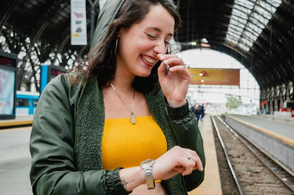 young latin woman of argentinian ethnicity dressed in yellow happily laughing out loud while standing on the platform waiting for the train to leave on a trip