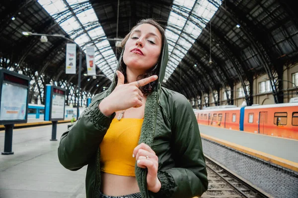 portrait of a young Latina woman of Argentinian ethnicity traveling with white skin, dressed in yellow and a green jacket, with a great attitude standing on the platform looking at the camera.