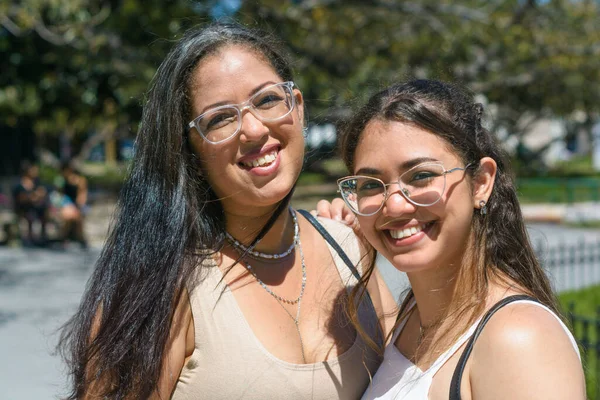portrait of two young latina tourist women of venezuelan ethnicity, mother and daughter standing on the street at noon during a walk, looking at the camera and smiling. lifestyle concept.