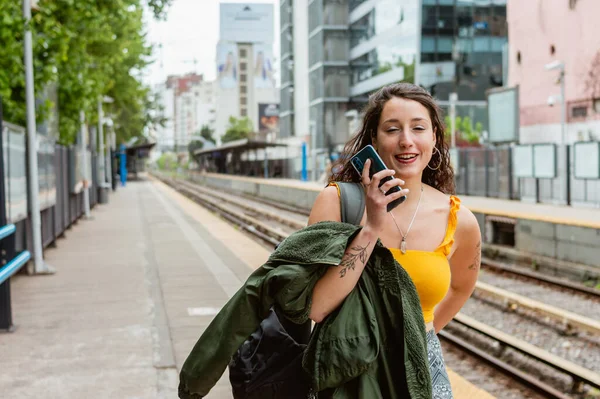 young latina woman of argentinian ethnicity, is walking along the train platform towards the exit and sending a voice note on the phone letting her know that she has arrived.