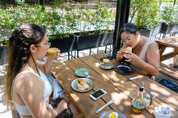 young Latina mother and daughter of Venezuelan ethnicity, sitting eating breakfast one weekend in a restaurant in Buenos Aires.