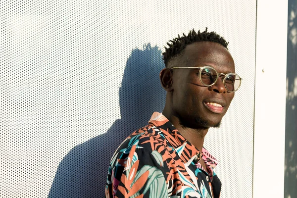 confidence, security and self esteem, young african man, with glasses and short hair, stands outdoors, smiles looking at the camera, copy space.