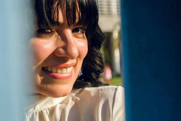 closeup portrait of young latina, venezuelan woman at sunset, in a public park, looking at the camera through blue walls.