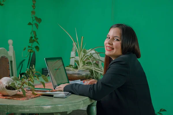 young latin business woman, person of argentinian ethnicity in formal wear, sitting at home with her laptop, looking at the camera smiling mischievously, business concept, copy space.
