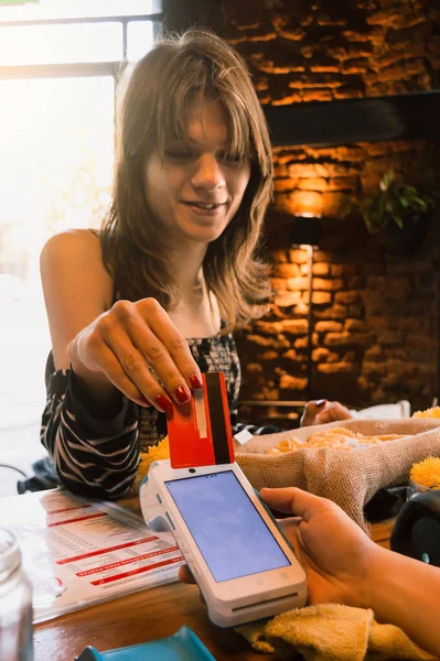 vertical image of a Latina transgender woman of Argentinian ethnicity, standing at the counter of a restaurant paying with her magnetic debit card