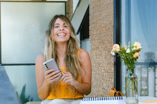 portrait of young latina woman of colombian ethnicity, with long hair and yellow clothes is sitting smiling and looking at the camera with the phone in her hand. technology concept, copy space.