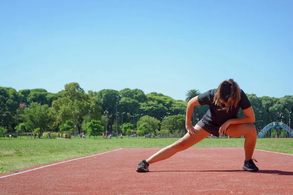 年轻的拉丁裔妇女 在跑道上做髋关节和腿侧伸 为健康的身体进行训练 — 图库照片
