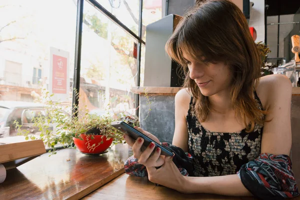 Latina transgender woman alone, sitting using the phone sitting in a restaurant, browsing the internet, using applications and social networks.