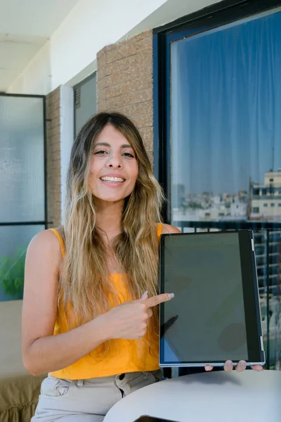 若いラテン語のビジネス女性コロンビアの民族性の垂直画像は カメラを見て座って笑顔ノートパソコンの画面を指してカメラを見て コピースペース — ストック写真