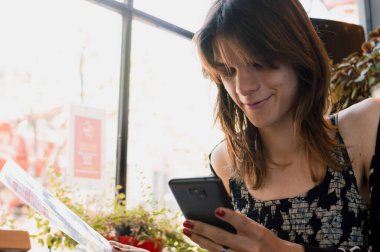 Genç transseksüel Latin kadının telefon kullanarak ve restoran menüsünü okuyarak yakın plan fotoğrafı..