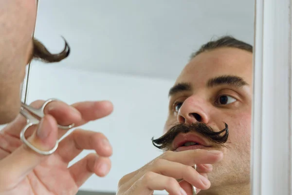 stock image personal hygiene, mustache trimming with scissors, young gender non-binary latino person in bathroom