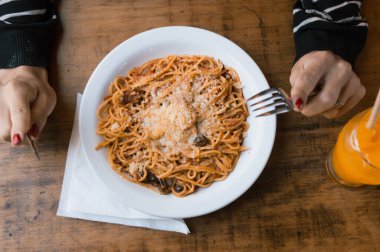 Elinde çatal bıçak takımı, masada bir tabak spagetti, yemek konsepti ve fotokopi alanı olan tanınmamış insanların üst görüntüsü..