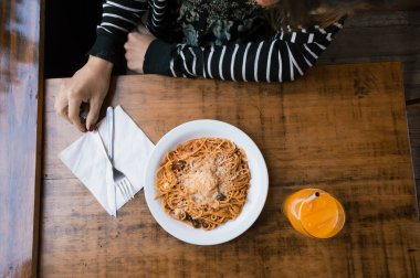 Bir tabak spagetti, portakal suyu, restoran konsepti, fotokopi odası yemek üzere olan bir masada tanınmayan birinin kolunun üst görüntüsü..