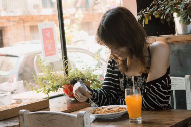 Portakal suyuyla makarna yiyen genç transseksüel kadın, pencere kenarında bir restoranda oturuyor, fotokopi odası, restoran konsepti..