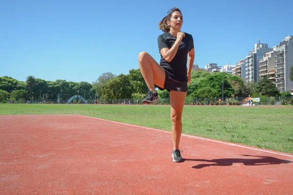 年轻的拉丁裔女子 身穿黑色运动服 将弯曲的腿举到一边 旋转髋关节 进行训练 健康生活概念 复制空间 — 图库照片