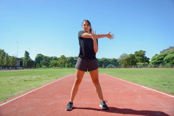 观看年轻的拉丁女子在运动赛道上训练 手臂伸展 站在跑道上热身准备跑 — 图库照片