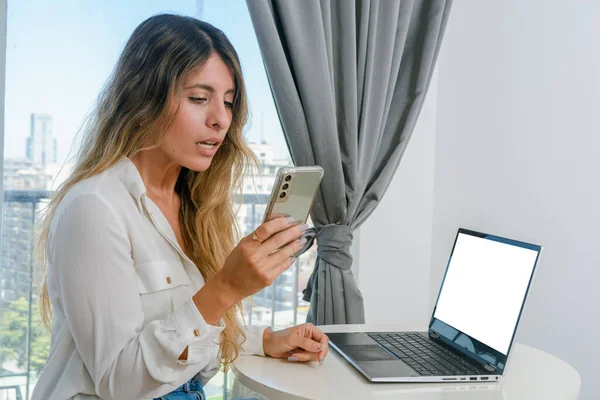 若いラテン系コロンビア人女性起業家は彼女の携帯電話の経済的利益を見て驚いた彼女のラップトップ ビジネスコンセプト コピースペースでオンラインで働いて — ストック写真
