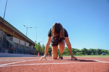 Yarış pistindeki kadının ön görünümü başlangıç konumunda, arkaplanda gökyüzü ve boşluğu kopyala.