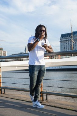 Rastalı ve koyu gözlüklü genç Afrikalı turist Buenos Aires 'te Puerto Madero' daki hendeğin yanında dinleniyor..