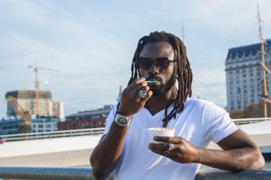 Rastalı, sakallı ve güneş gözlüklü zenci bir adamın portresi. Dinlenmiş ve dondurma yiyor. Gün batımında Buenos Aires 'te hafta sonunun tadını çıkarıyor..