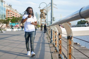 Rastalı, sakallı ve gözlüklü genç siyahi adam, haftasonu gün batımının tadını çıkarıyorsun, Buenos Aires 'te, Puerto Madero mahallesinde dondurma yiyorsun..