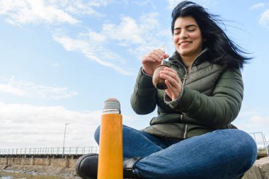 Genç Latin kadın soğuk bir günde dışarıda oturuyor, sabah keyfine bakıyor. Yerba eşleri, yaşam tarzı konsepti, fotokopi alanı..