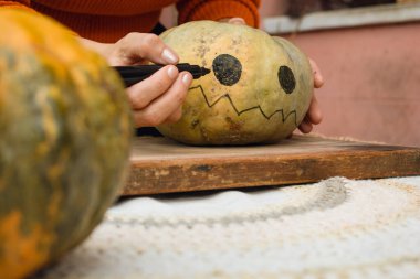 Ahşap kesim tahtasına cadılar bayramı gecesi için balkabağı çizen tanınmayan beyaz kadın elleri, el sanatları konsepti, kopyalama alanı