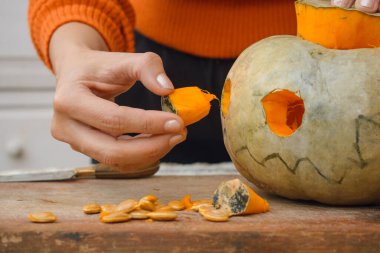 Tanımlanamayan beyaz kadın ellerinin ahşap kesim tahtasının üzerinde balkabağı gözü yapmak için porsiyon söküp Cadılar Bayramı 'nda süslediği yakın plan.