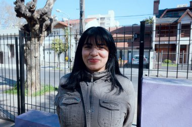 Utangaç siyah saçlı, Venezuelalı, gri ceketli bir kadının portresi. Parkta durmuş kameraya bakıyor. Gülme dürtüsü, yaşam tarzı konsepti..