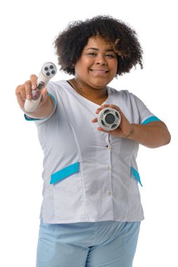 dikey görüntü genç afro Latin kadın üniforma giyiyor, kameraya bakıyor gülümsüyor ve cilt temizleme aletlerini gösteriyor.